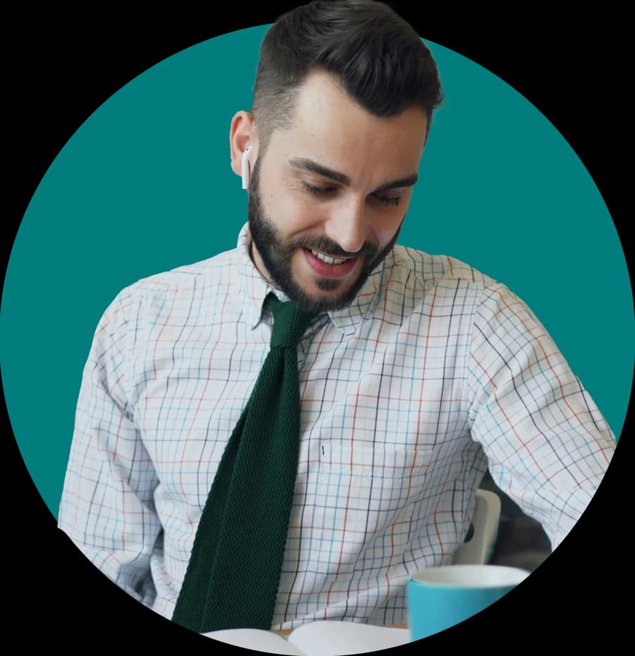 Ein lächelnder Mann mit Ohrhörer liest an seinem Schreibtisch.
